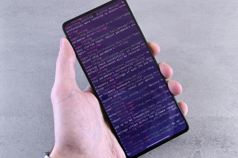 Hand holding a smartphone showing app code on its screen